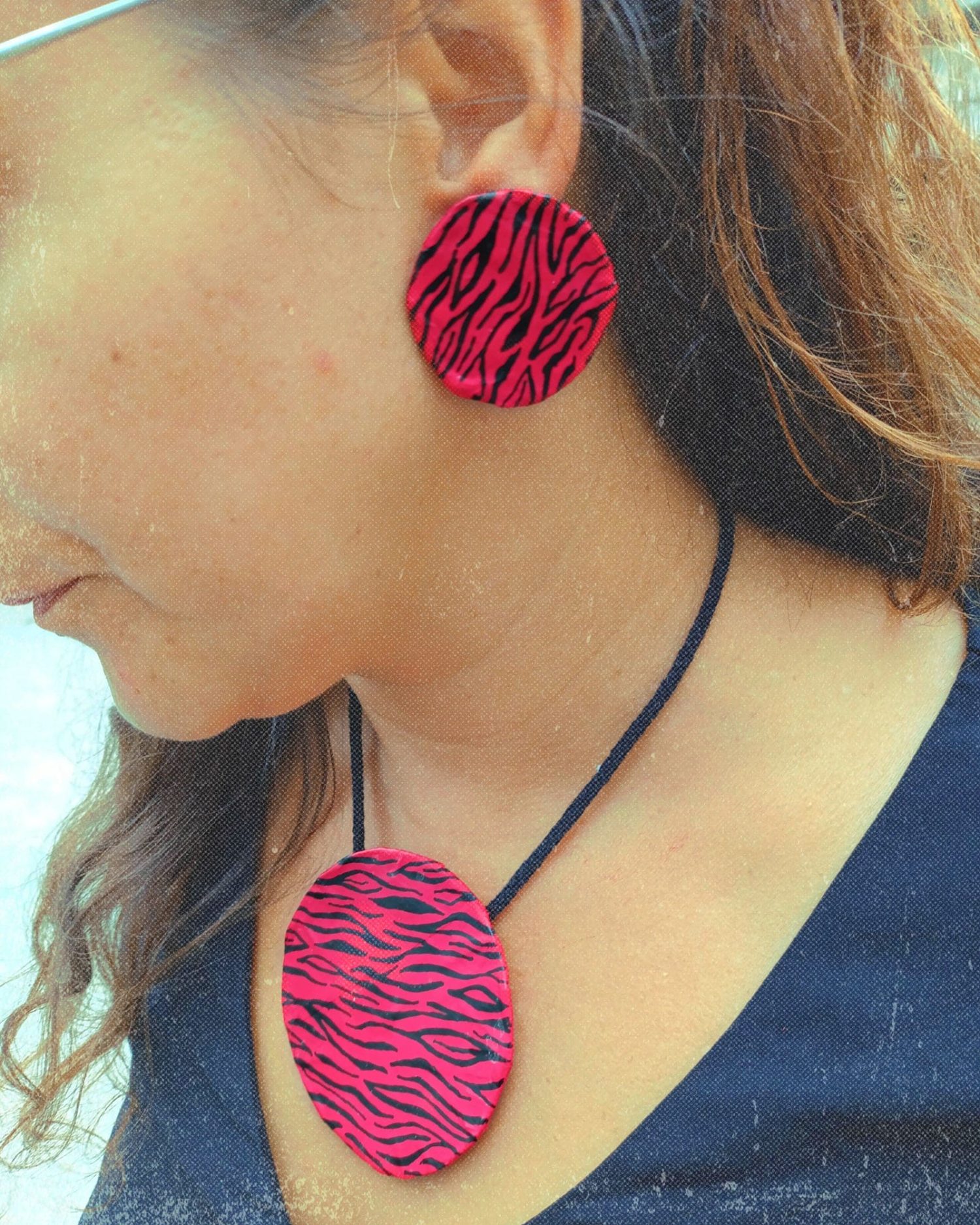 Modelo llevando conjunto Sahara: pendientes redondos y collar con estampado de cebra sobre fondo rojo