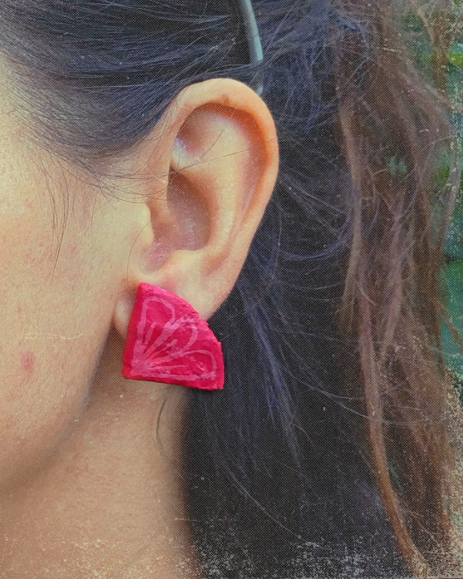 Modelo llevando pendientes Aurora en tonos rojos con motivos florales y forma de cuarto de circunferencia