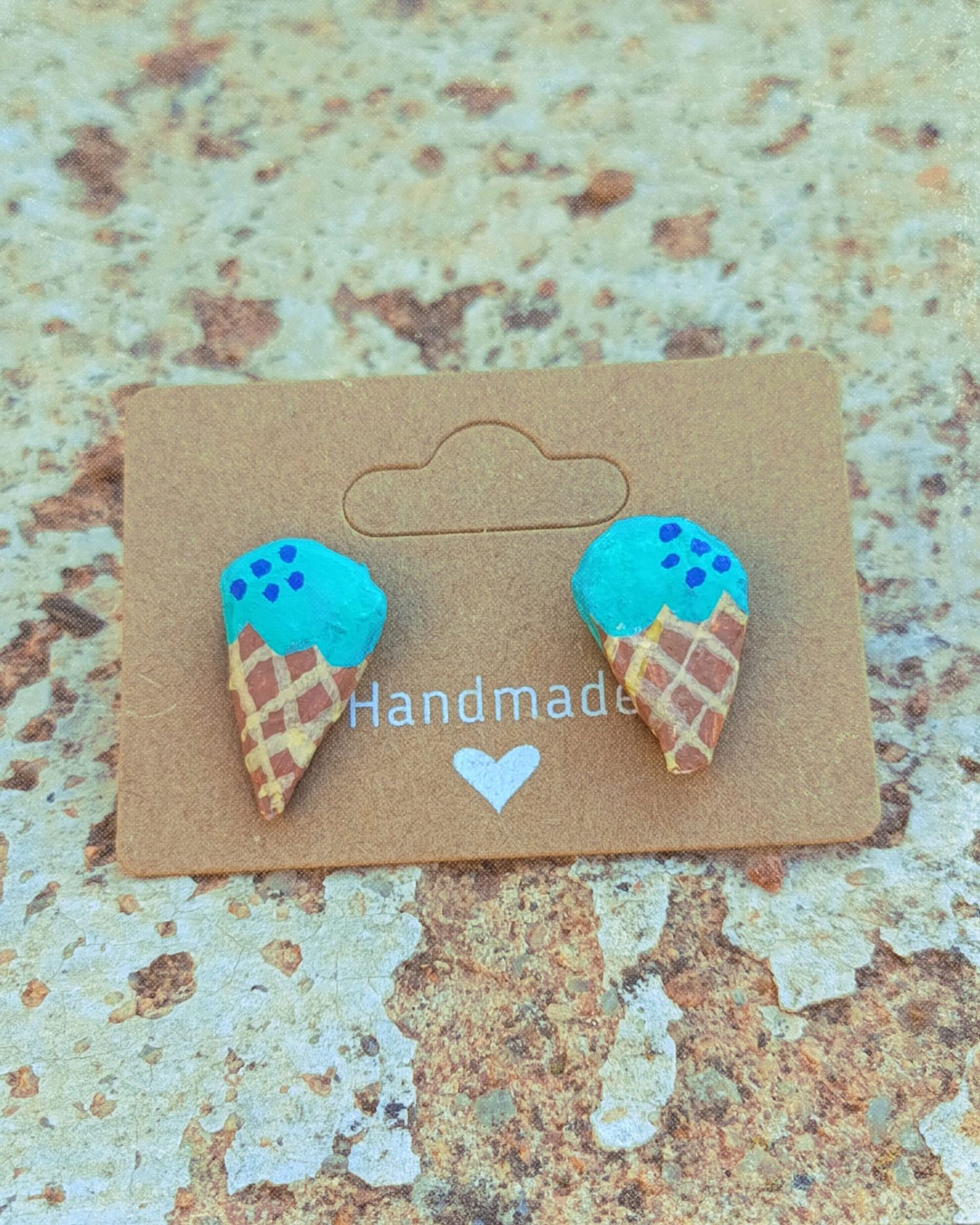 Pendientes infantiles con forma de helado sobre packaging de cartón colocados sobre fondo de piedra